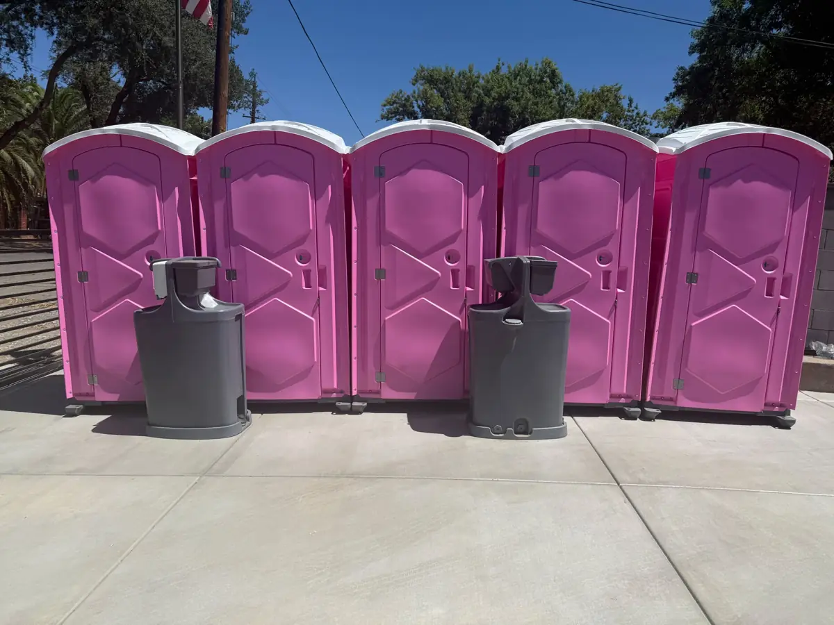 Five pink porta potties with two handwashing stations set up on concrete