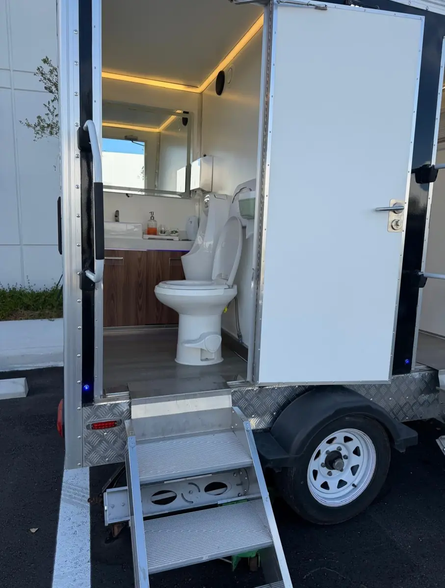Restroom trailer with door open showing lit interior and steps